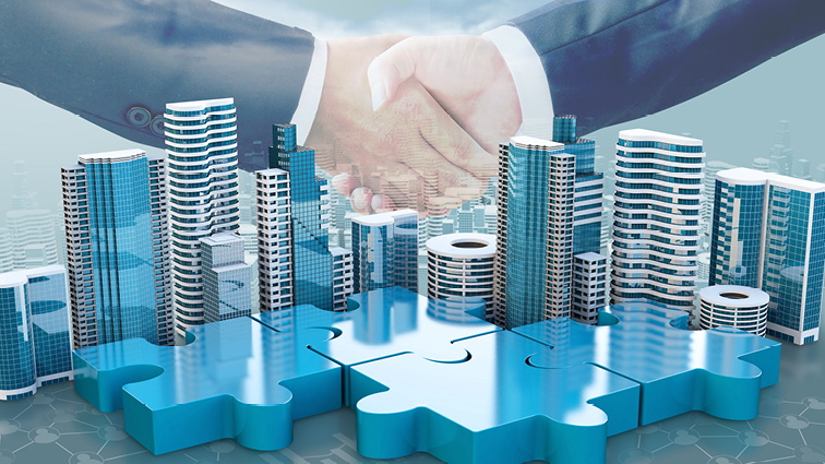 Two men in suits shaking hands over a city of skyscrapers with puzzle pieces in front of them.