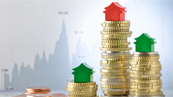 Stacks of gold coins with red and green wooden houses atop and a rising and falling chart in the background.