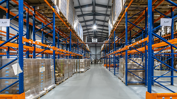 The interior of a warehouse with green and orange shelves stacked with pallets of goods.