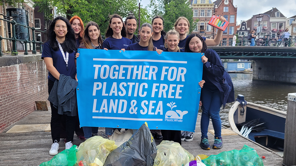 The WPC Amsterdam team standing beside a canal with a 'Together for Plastic Free Land & Sea' sign
