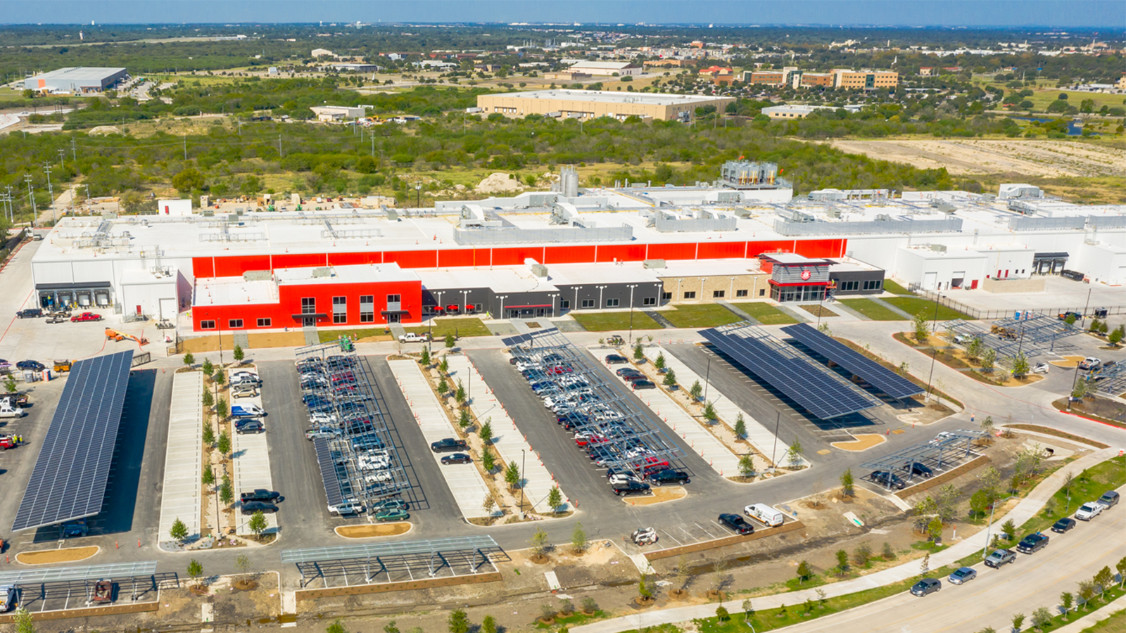 Aerial photo of a large, red industrial facility with a parking lot solar panels.