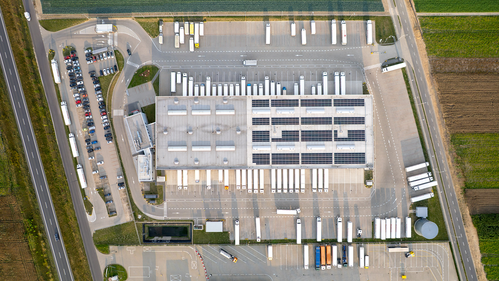 Aerial photo of a property with many 18-wheeler trucks, solar panels covering the majority of the website and green fields