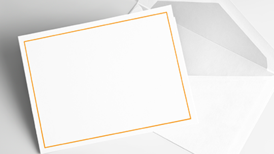 White card with gold trim laying on a white envelope with a gray background