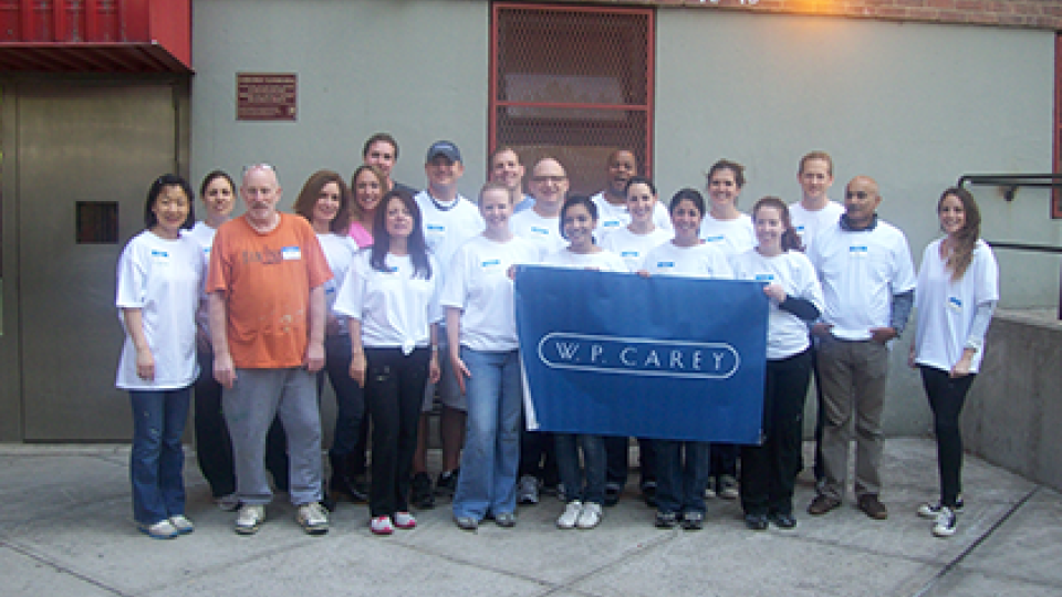 W. P. Carey employees in white shirts holding a navy WPC flag