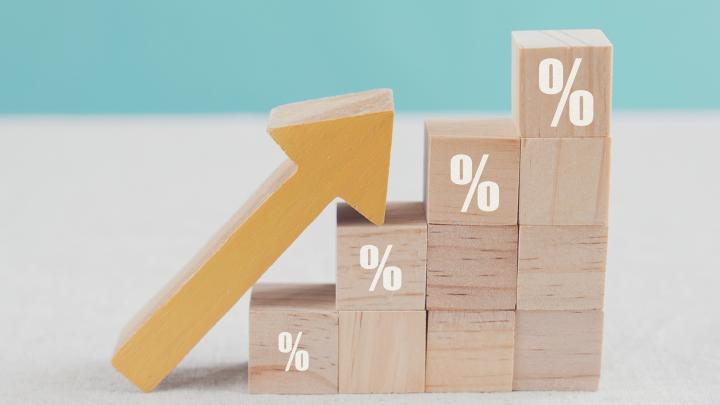 Wooden blocks stacked like stairs, percentage signs are on the top block in each column, a wooden arrow lies on the blocks pointing up to the top block