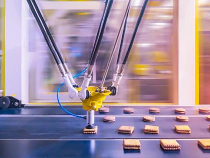 A robotic arm makes sandwich cookies on a conveyer belt