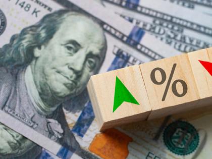 Three wooden blocks sitting on top of stack of $100 bills. The first block has a green arrow pointing up, the second block has a percentage sign, the third block has a red arrow pointing down.