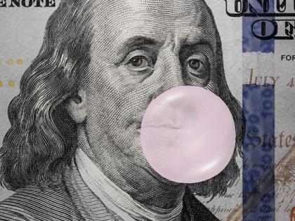 Tight shot of a $100 bill with Benjamin Franklin blowing a bubble of pink bubble gum