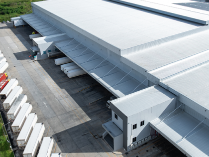 Exterior of a white warehouse with white trucks at the docking stations. 