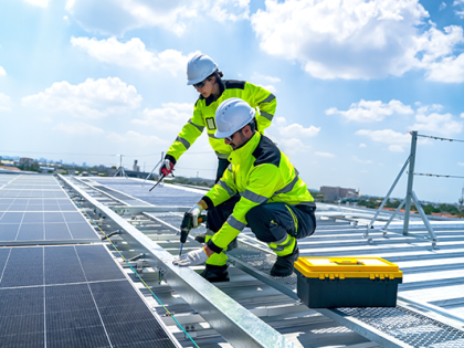 Two workers in reflective gear on a rooftop covered in solar panels.