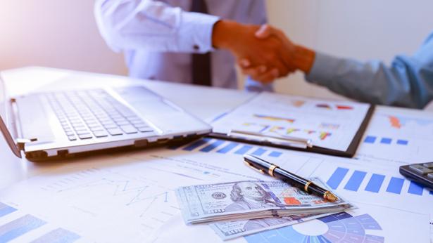 Financial documents on a table while people shake hands over recession-proofing their commercial net-leased real estate investment properties and portfolios