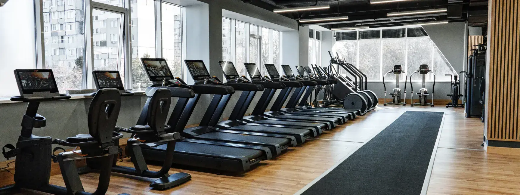 A gym with rows of treadmills and large windows