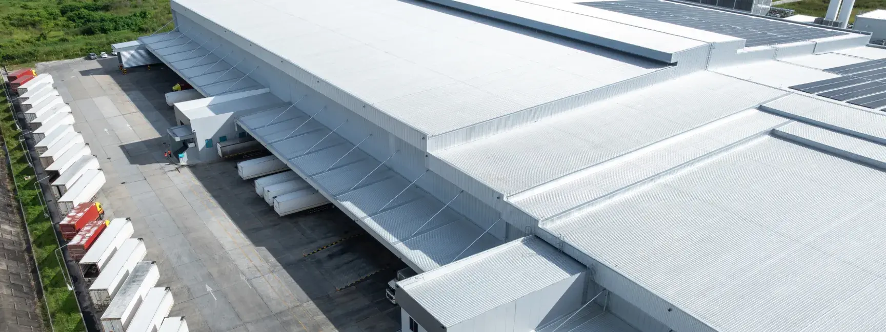 Exterior of a white warehouse with white trucks at the docking stations. 