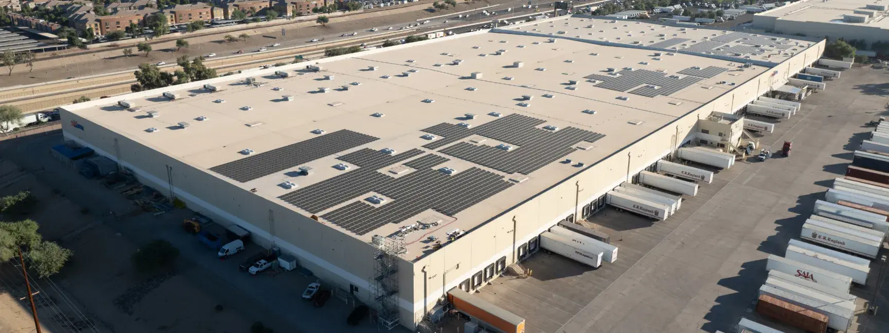 An aerial photo of a large industrial facility, with a white roof with solar panels on about half of it.